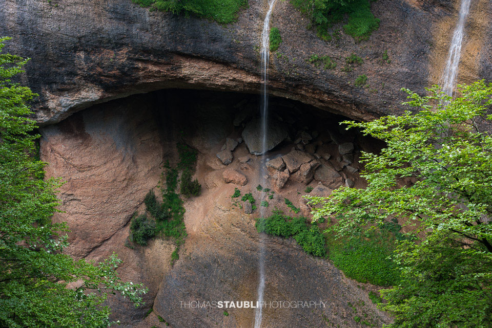 Ein Wasserfall fällt aus einer natürlichen Felsnische über Geröll und Felsen in die bewaldete Necker-Schlucht – wildromantische Kulisse beim Ofenloch.