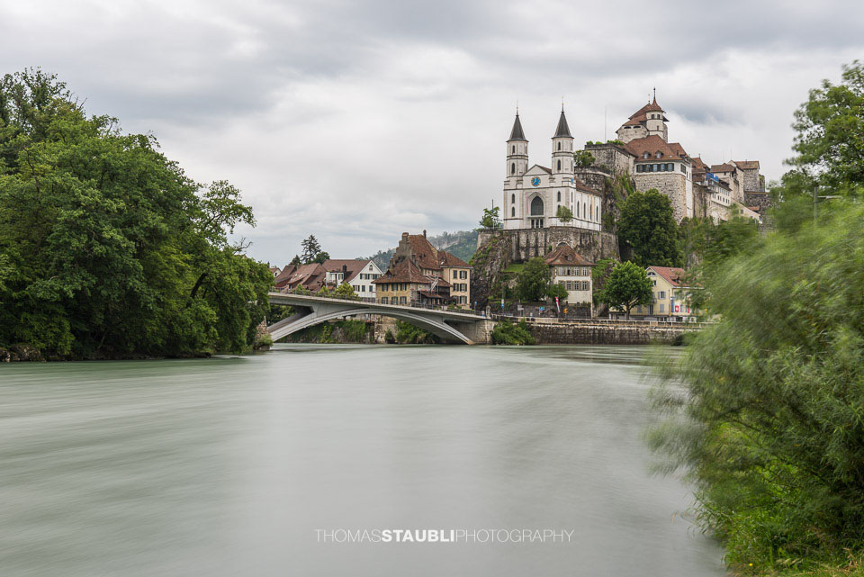 Blick auf die historische Festung Aarburg, die auf einem markanten Felsen über der Aare thront, mit der Altstadt am Flussufer.