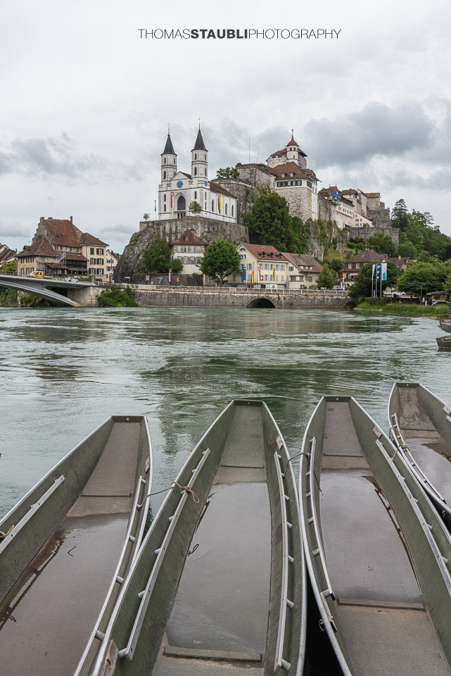 Die Festung Aarburg und die reformierte Kirche erheben sich eindrucksvoll über dem Fluss, während im Vordergrund mehrere Weidlinge am ruhigen Ufer liegen.