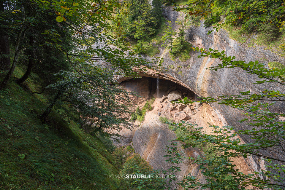 Ein Wasserfall fällt aus einer natürlichen Felsnische über Geröll und Felsen in die bewaldete Necker-Schlucht – wildromantische Kulisse beim Ofenloch.
