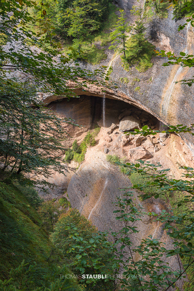 Ein Wasserfall fällt aus einer natürlichen Felsnische über Geröll und Felsen in die bewaldete Necker-Schlucht – wildromantische Kulisse beim Ofenloch.