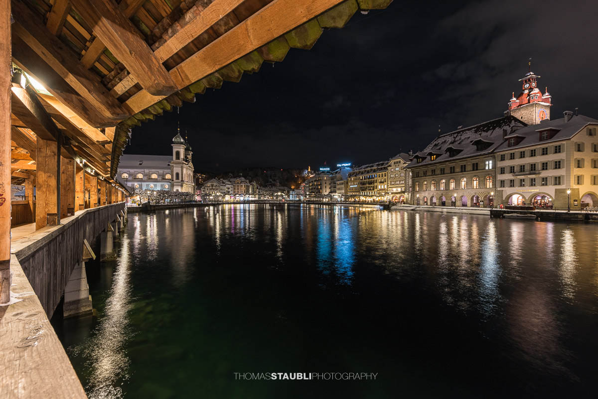 Abendlicher Blick von der Kapellbrücke in Luzern mit erleuchteten Fassaden, der Jesuitenkirche und der Reuss im Vordergrund
