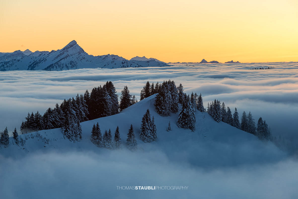 Winterliche Berglandschaft mit schneebedecktem Hügel, Nebelmeer und orangefarbenem Abendhimmel am Kronberg