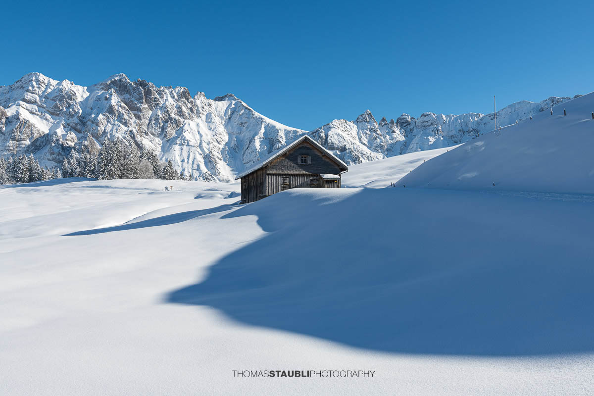Winterliche Berghütte mit Alpstein im Hintergrund unter strahlend blauem Himmel
