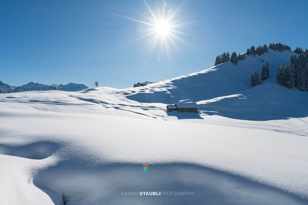Winterliche Berghütte mit dem Pfingstboden im Hintergrund unter strahlend blauem Himmel