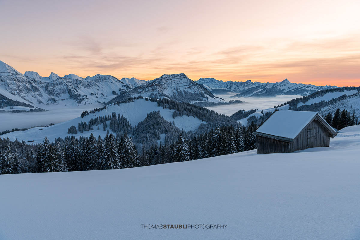 Verschneite Berghütten in den Schweizer Alpen bei Sonnenuntergang mit beeindruckender Bergkulisse