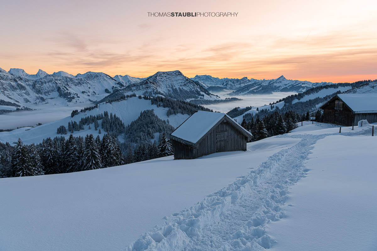 Verschneite Berghütten in den Schweizer Alpen bei Sonnenuntergang mit beeindruckender Bergkulisse