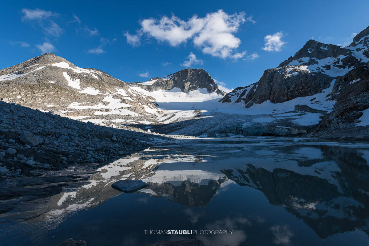 Gletschersee des Witenwasserengletschers, im Hintergrund vor blauem Himmel mit Schönwetterwolken der Hüenerstock und Witenwasserenstock in der Abendsonne.