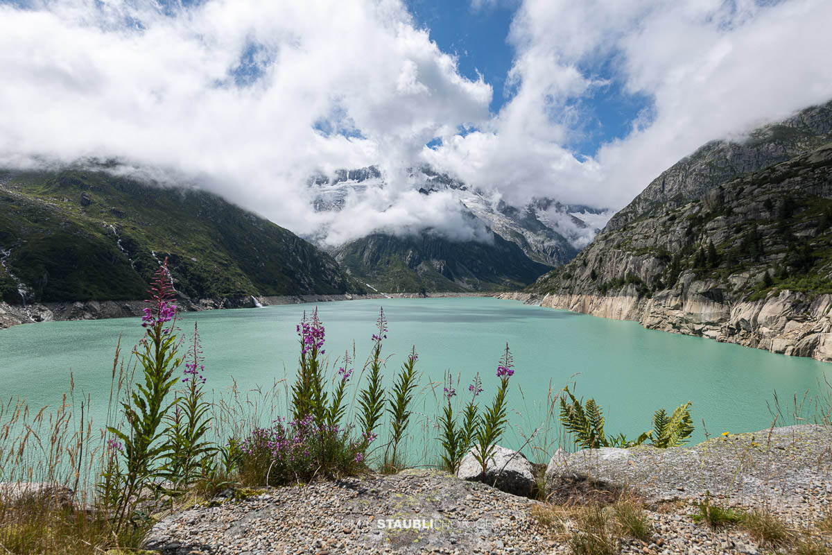 Blick vom Göscheneralpsee im Kanton Uri zum wolkenverhangenen Winterbergmassiv mit Gletscher und steilen Felsflanken.