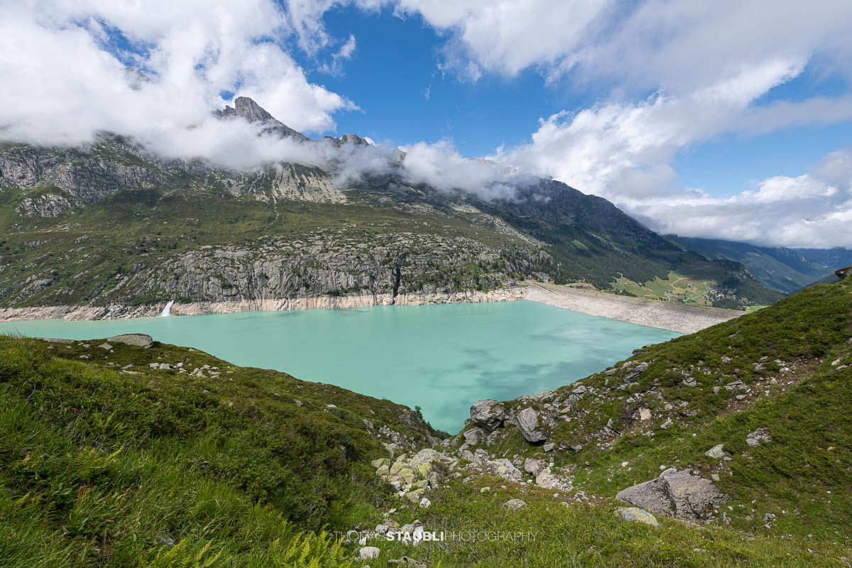 Blick über den türkisblauen Göscheneralpsee im Göschenertal, umgeben von steilen Felswänden und grünen Berghängen im Kanton Uri.