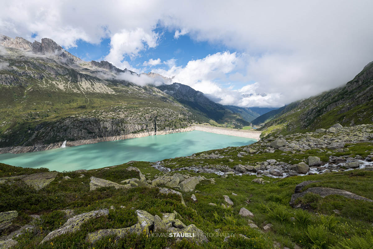 Blick über den türkisblauen Göscheneralpsee im Göschenertal, umgeben von steilen Felswänden und grünen Berghängen im Kanton Uri.