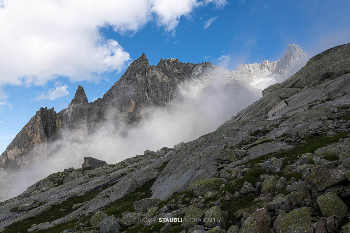 Felsige Älprigenplatten im Vordergrund, dahinter der spitze Gipfel des Feldschijen, teilweise von Nebelschwaden umgeben, unter blauem Himmel in den Urner Alpen.