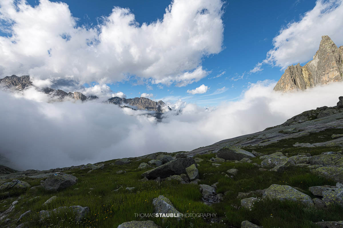 Felsige Landschaft der Älprigenplatten mit Aussicht ins Göschenertal, von Nebelschwaden durchzogen, umgeben von schroffen Gipfeln unter blauem Himmel.