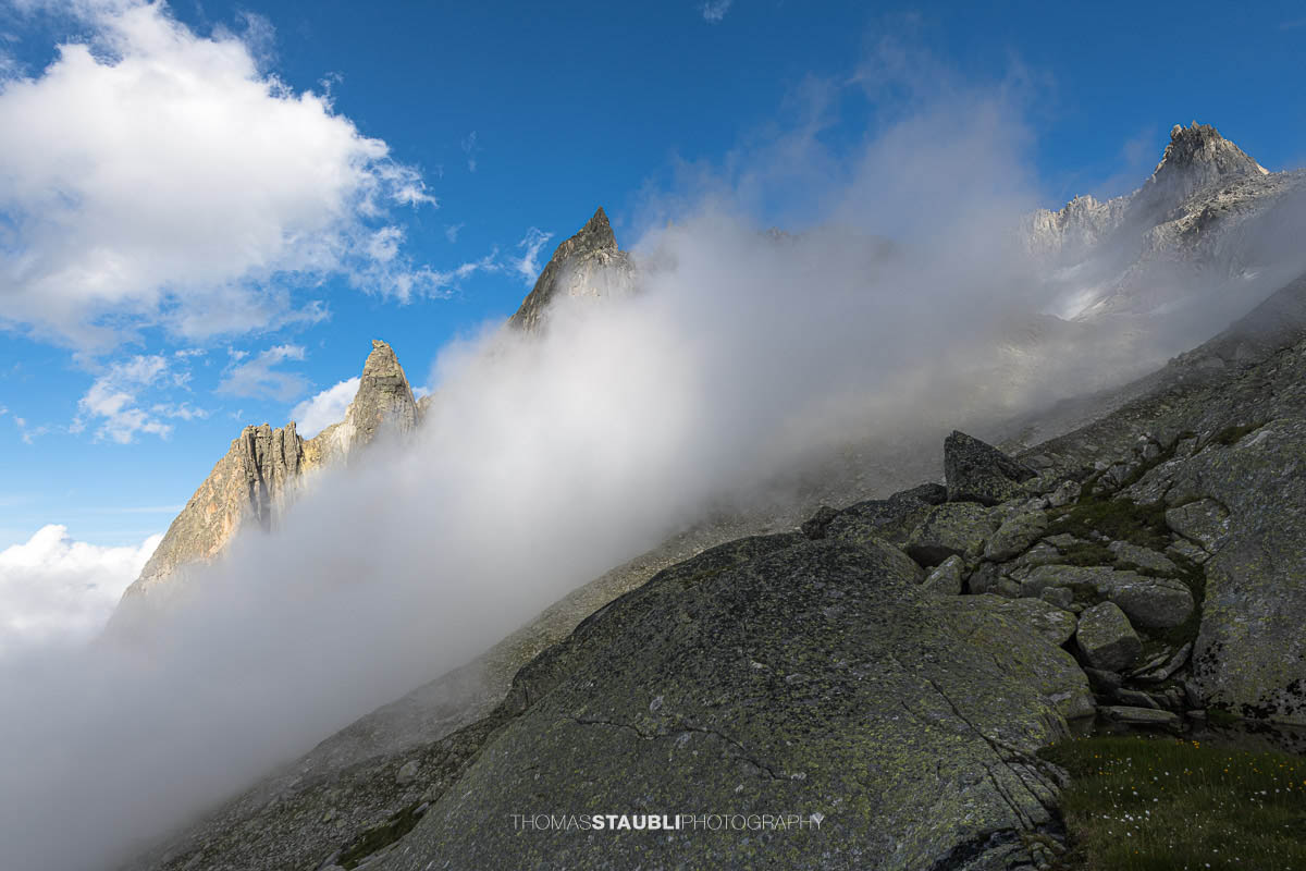 Felsige Älprigenplatten im Vordergrund, dahinter der spitze Gipfel des Feldschijen, teilweise von Nebelschwaden umgeben, unter blauem Himmel in den Urner Alpen.