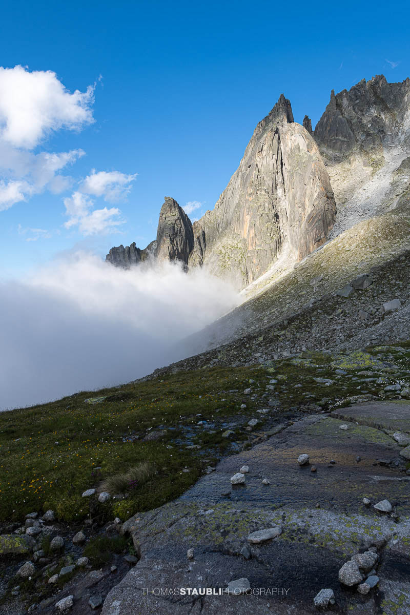 Felsige Älprigenplatten im Vordergrund, dahinter der spitze Gipfel des Feldschijen, teilweise von Nebelschwaden umgeben, unter blauem Himmel in den Urner Alpen.
