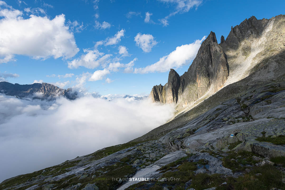 Felsige Älprigenplatten im Vordergrund, dahinter der spitze Gipfel des Feldschijen, teilweise von Nebelschwaden umgeben, unter blauem Himmel in den Urner Alpen.