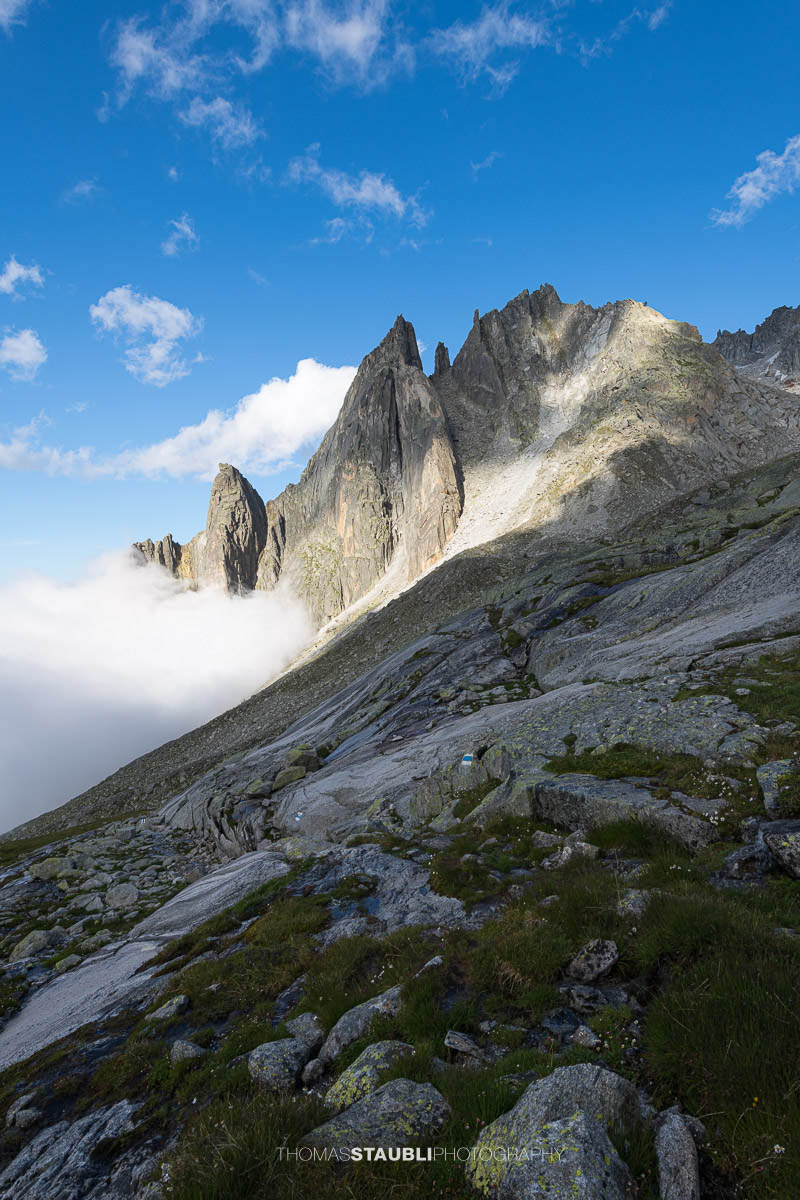 Felsige Älprigenplatten im Vordergrund, dahinter der spitze Gipfel des Feldschijen, teilweise von Nebelschwaden umgeben, unter blauem Himmel in den Urner Alpen.