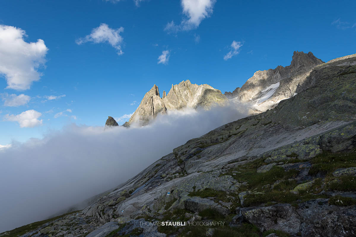 Felsige Älprigenplatten im Vordergrund, dahinter der spitze Gipfel des Feldschijen, teilweise von Nebelschwaden umgeben, unter blauem Himmel in den Urner Alpen.