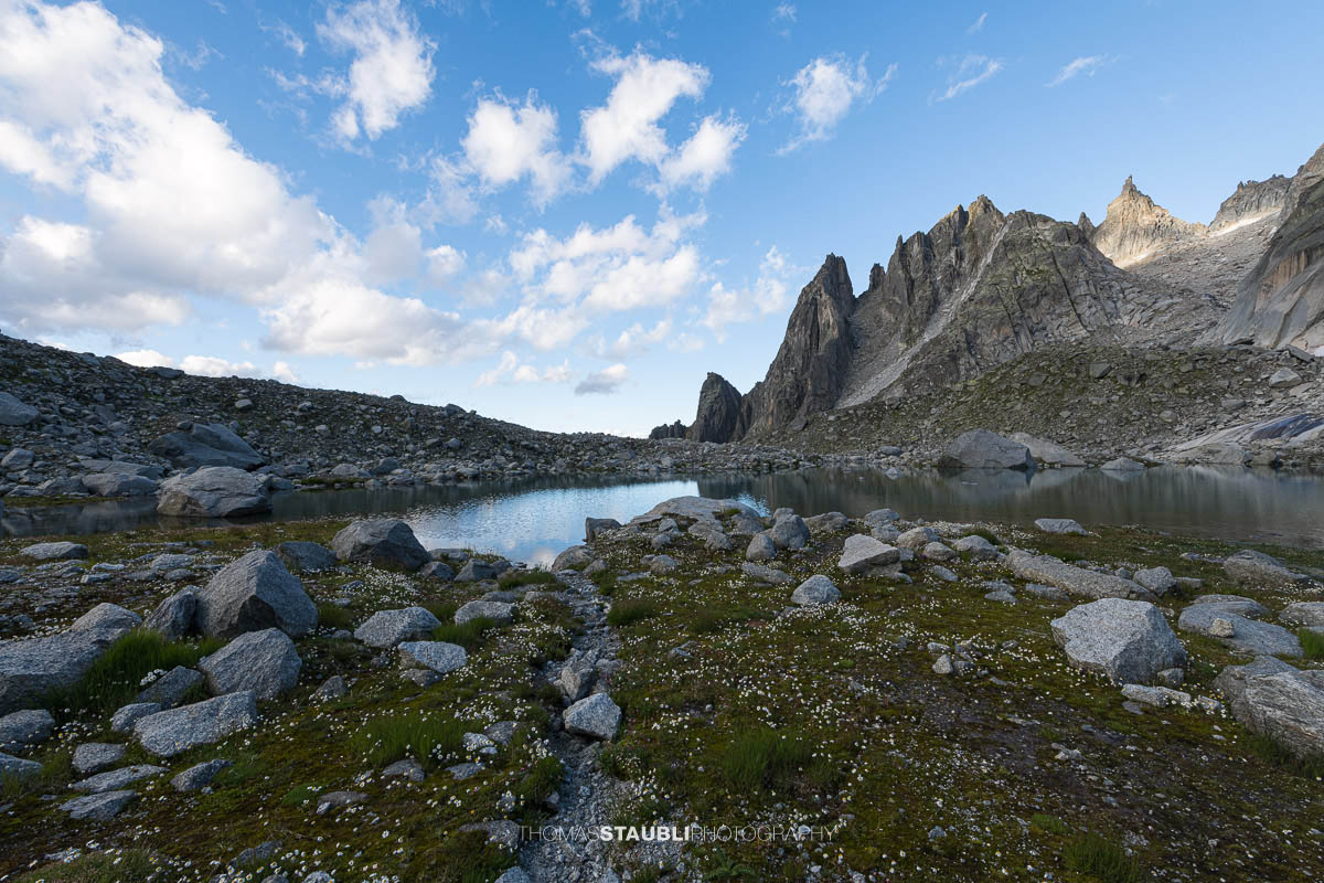 Älprigensees im Göschenertal mit Blick zu der schroffen Felsschijen-Gipfel unter blauem Himmel mit Wolken.