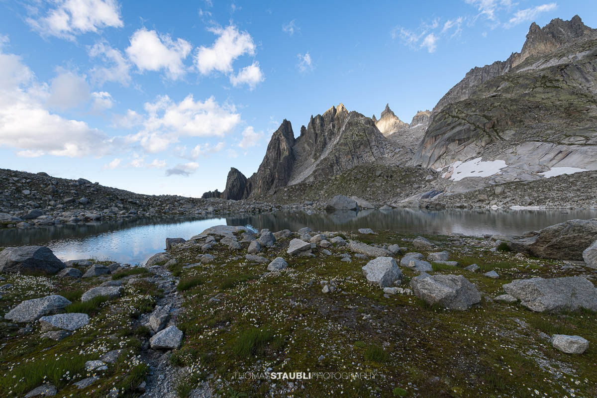 Älprigensees im Göschenertal mit Blick zu der schroffen Felsschijen-Gipfel unter blauem Himmel mit Wolken.