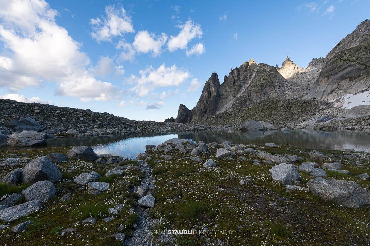 Älprigensees im Göschenertal mit Blick zu der schroffen Felsschijen-Gipfel unter blauem Himmel mit Wolken.