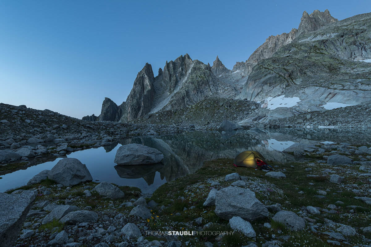 Beleuchtetes Zelt am Ufer des Älprigensees im Göschenertal bei Nacht, dahinter die schroffen Felsschijen-Gipfel im Mondlicht