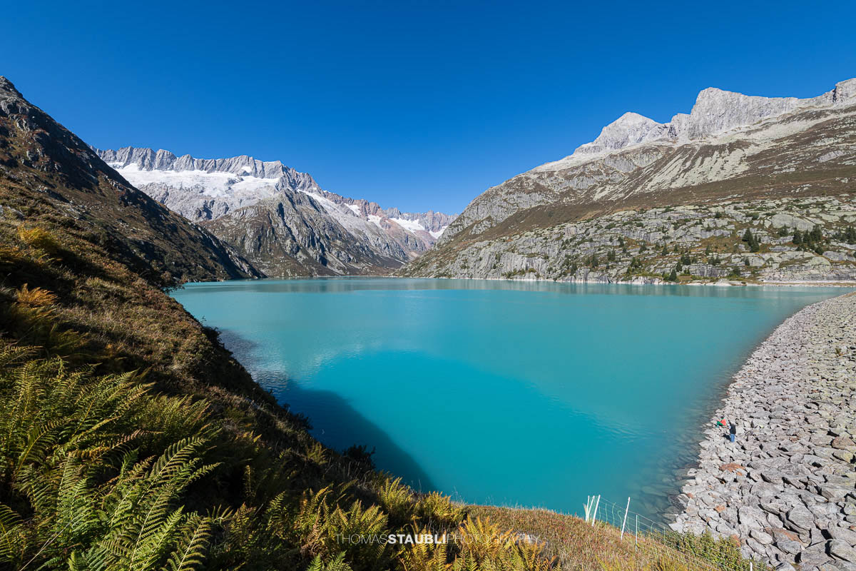 Blick über den türkisfarbenen Göscheneralpsee im Kanton Uri, umrahmt von steilen Felsflanken und den schneebedeckten Gipfeln des Dammastockmassivs im Hintergrund.