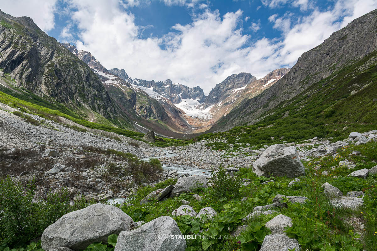 Blick durch das Chelenalptal im Kanton Uri, wo der Chelenreuss zwischen Geröllfeldern und alpiner Vegetation talwärts fliesst, während im Hintergrund der Chelengletscher unterhalb des Winterbergmassivs liegt.