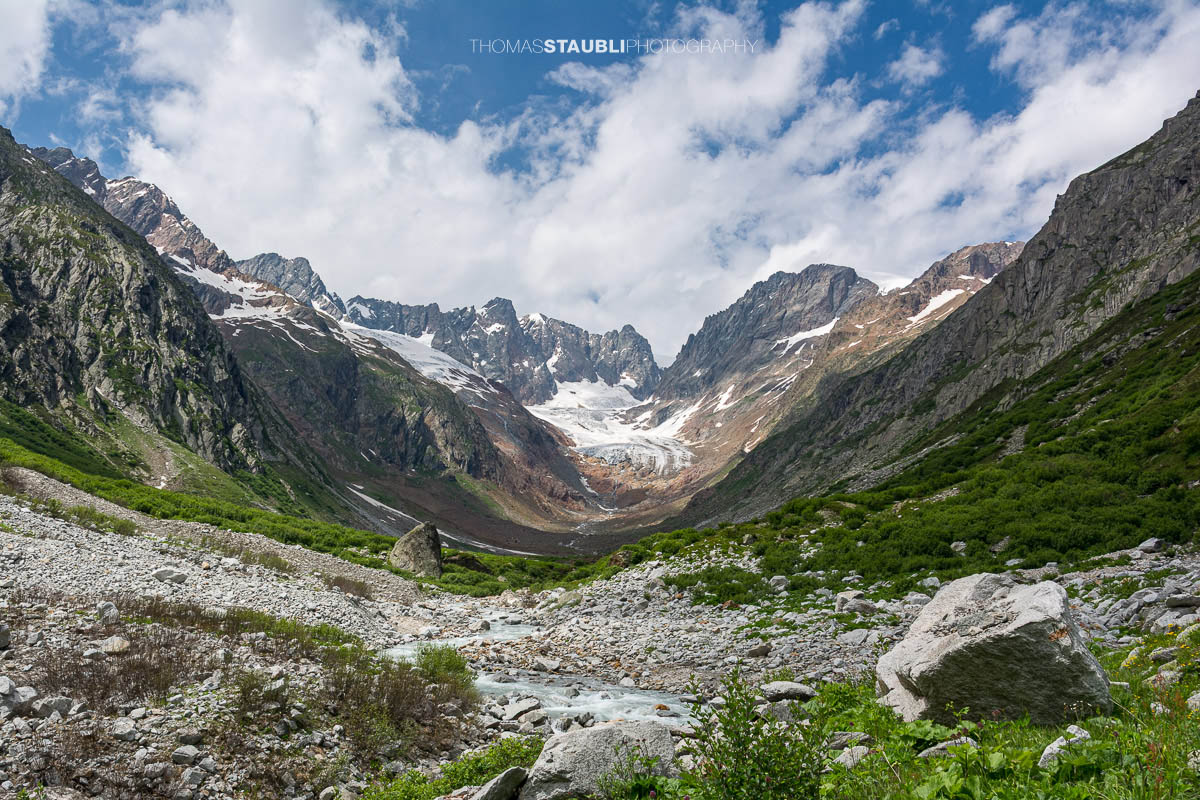 Blick durch das Chelenalptal im Kanton Uri, wo der Chelenreuss zwischen Geröllfeldern und alpiner Vegetation talwärts fliesst, während im Hintergrund der Chelengletscher unterhalb des Winterbergmassivs liegt.
