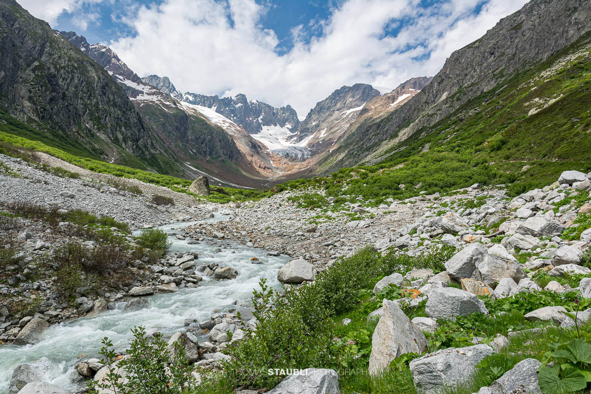 Blick durch das Chelenalptal im Kanton Uri, wo der Chelenreuss zwischen Geröllfeldern und alpiner Vegetation talwärts fliesst, während im Hintergrund der Chelengletscher unterhalb des Winterbergmassivs liegt.