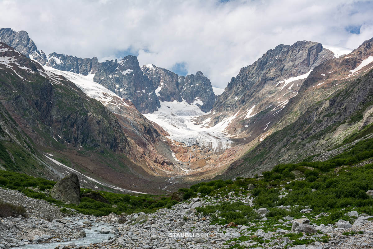 Blick durch das Chelenalptal im Kanton Uri, wo der Chelenreuss zwischen Geröllfeldern und alpiner Vegetation talwärts fliesst, während im Hintergrund der Chelengletscher unterhalb des Winterbergmassivs liegt.