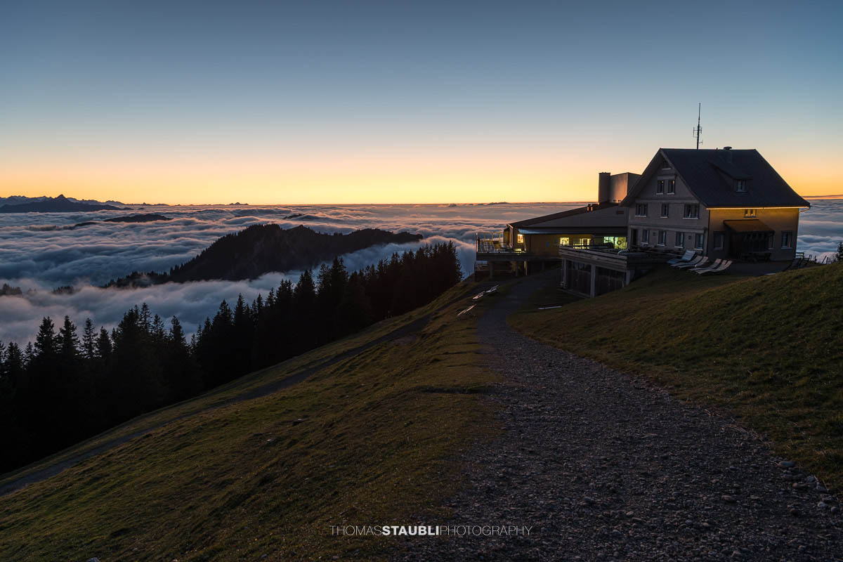 Warme Abendsonne taucht den Kronberg in goldenes Licht, während Nebelschwaden über den bewaldeten Hängen aufsteigen und sich ein stilles Nebelmeer über dem Appenzellerland ausbreitet.