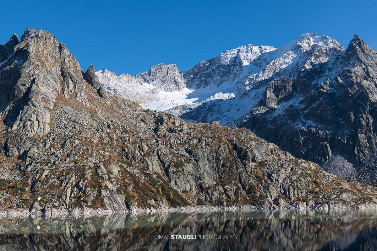 Die Albignahütte liegt auf einem Felsvorsprung, dahinter erheben sich die schroffen Gipfel und der Gletscher Vadrec dal Cantun in den Bergeller Alpen.