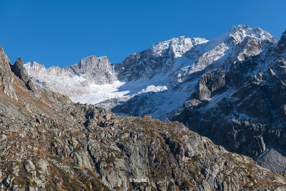 Die Albignahütte liegt auf einem Felsvorsprung, dahinter erheben sich die schroffen Gipfel und der Gletscher Vadrec dal Cantun in den Bergeller Alpen.