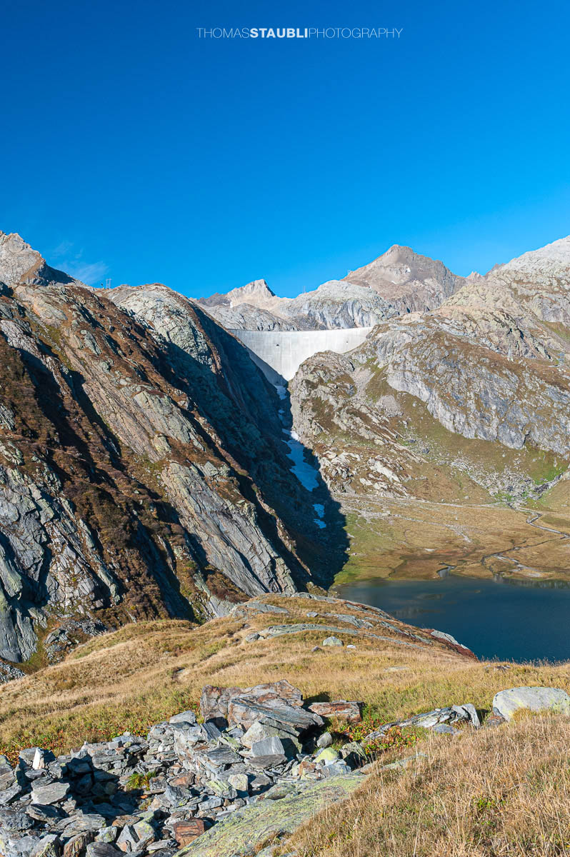 Lago Bianco im Hochgebirge des Tessins, im Hintergrund die Staumauer des Lago dei Cavagnöö in felsiger alpiner Landschaft.