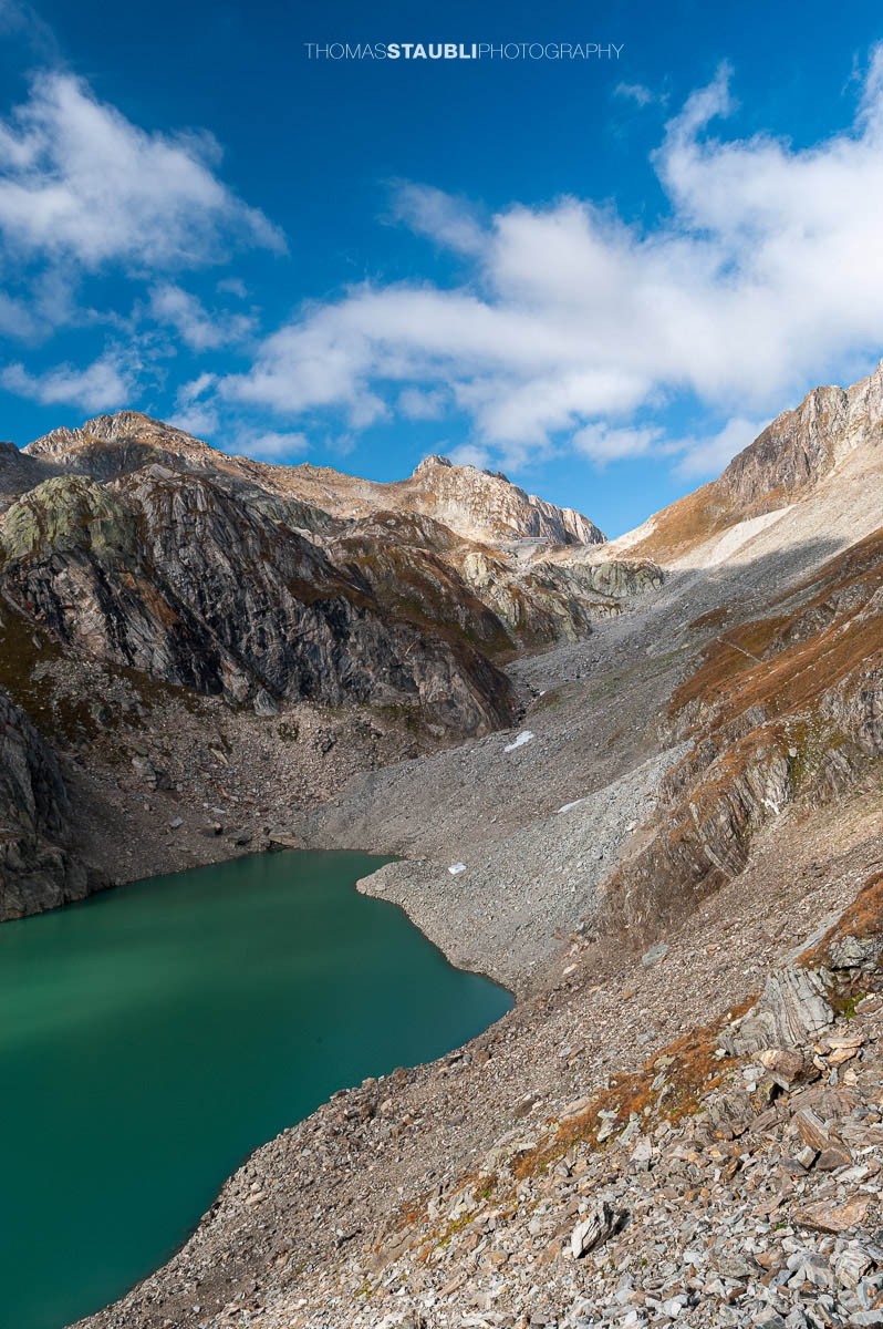 Lago Sfundau im hochalpinen Gelände des Tessins, darüber die Capanna Cristallina vor felsiger Gebirgslandschaft.
