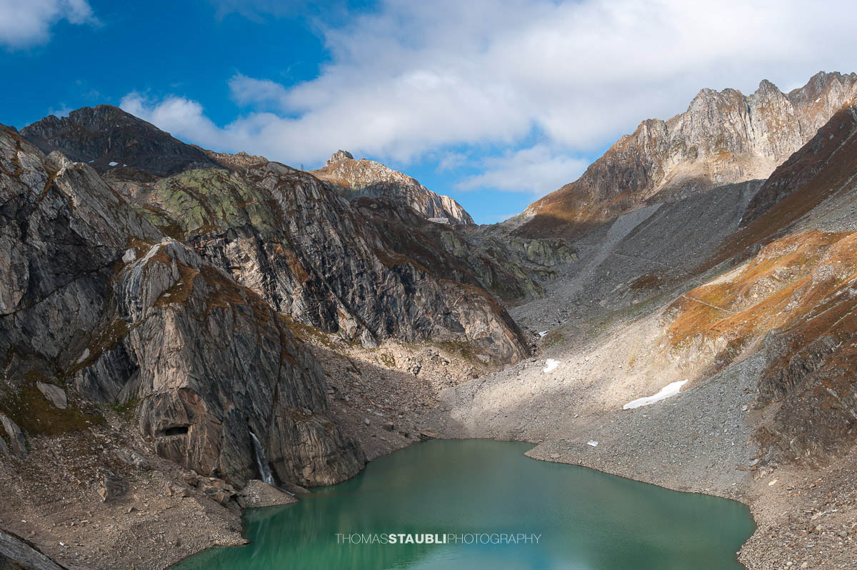 Lago Sfundau im hochalpinen Gelände des Tessins, darüber die Capanna Cristallina vor felsiger Gebirgslandschaft.
