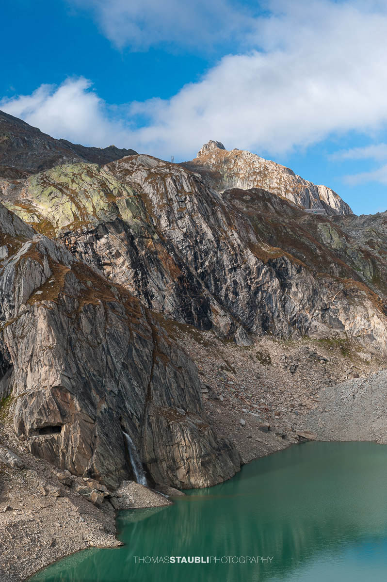 Lago Sfundau im hochalpinen Gelände des Tessins, darüber die Capanna Cristallina vor felsiger Gebirgslandschaft.