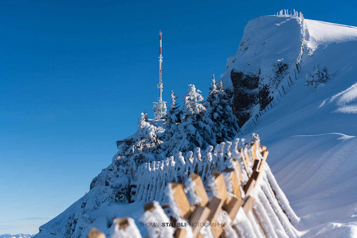 Verschneiter Rigi Kulm mit Schneezäunen, Gipfelantenne und klarem Winterhimmel in der Zentralschweiz.
