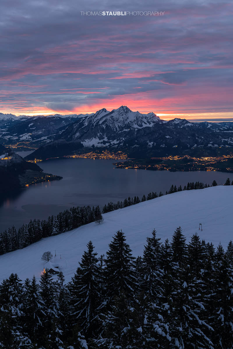 Winterlicher Blick auf den Vierwaldstättersee und den Pilatus im intensiven Abendrot unter einer dramatisch bewölkten Himmeldecke.
