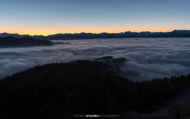 Blick vom Bachtel bei Hinwil in der Morgendämmerung gegen Osten, mit ausgedehntem Nebelmeer über der Ostschweiz und dunklen Hügelzügen im Vordergrund.