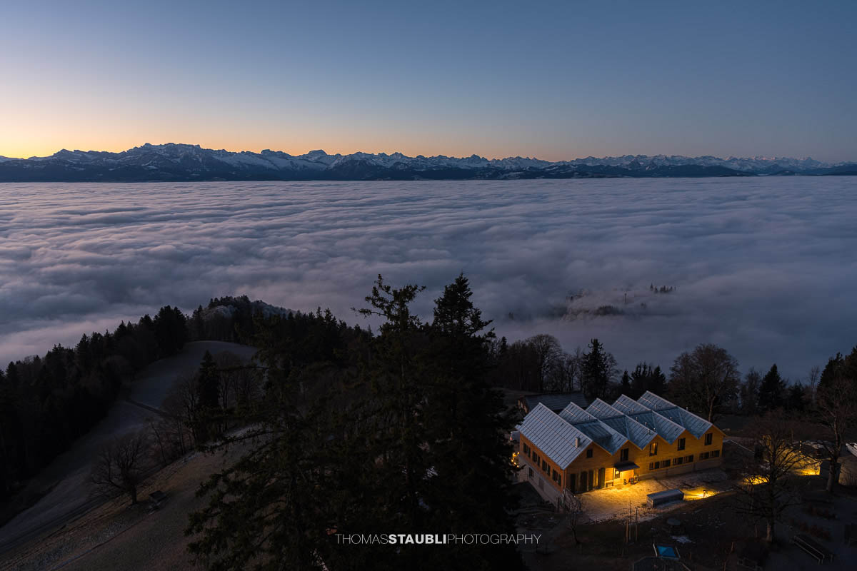 Blick vom Bachtel bei Hinwil in der Morgendämmerung gegen Osten, mit ausgedehntem Nebelmeer über der Ostschweiz und dunklen Hügelzügen im Vordergrund.