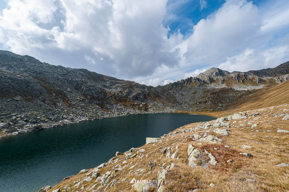 Lago d’Orsino am Gotthardpass, kleiner Hochgebirgssee mit ruhiger Wasserfläche, umgeben von steinigen Hängen und alpiner Vegetation.