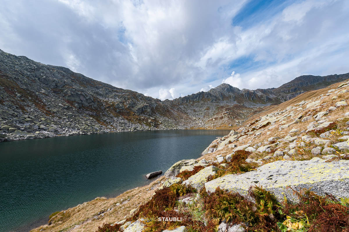 Lago d’Orsino am Gotthardpass, kleiner Hochgebirgssee mit ruhiger Wasserfläche, umgeben von steinigen Hängen und alpiner Vegetation.