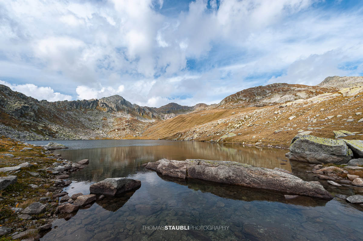 Lago d’Orsino am Gotthardpass, kleiner Hochgebirgssee mit ruhiger Wasserfläche, umgeben von steinigen Hängen und alpiner Vegetation.
