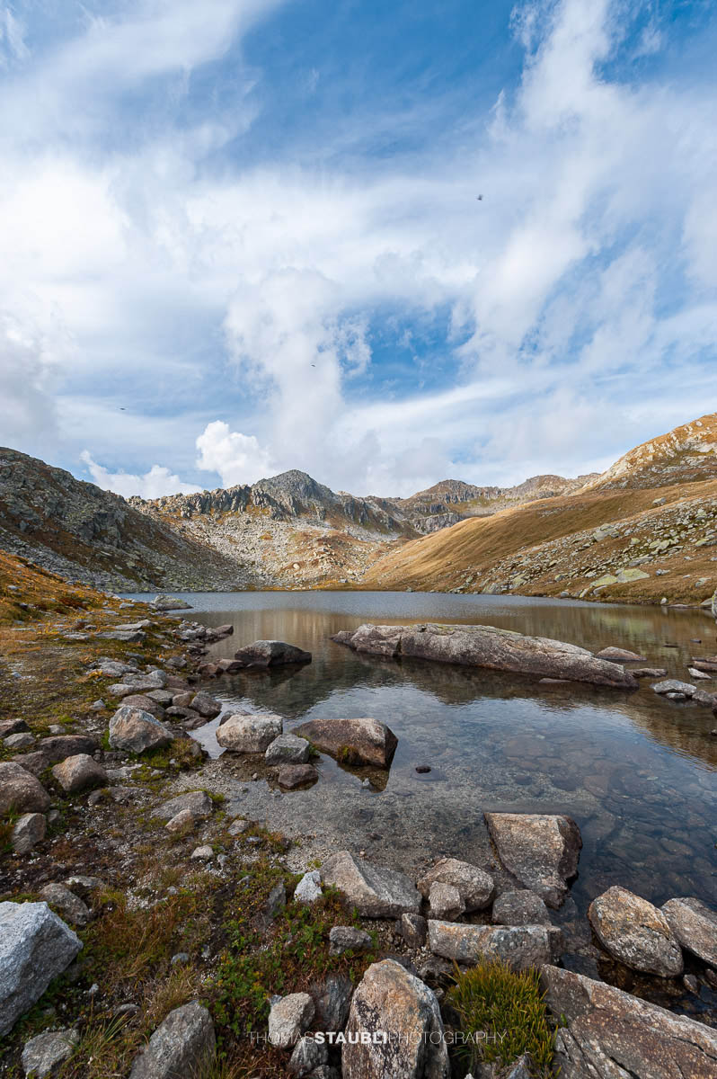 Lago d’Orsino am Gotthardpass, kleiner Hochgebirgssee mit ruhiger Wasserfläche, umgeben von steinigen Hängen und alpiner Vegetation.