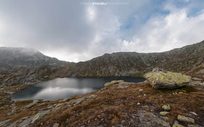 Laghi d’Orsirora nahe dem Gotthardpass, kleiner Hochgebirgssee in karger alpiner Felslandschaft unter wechselndem Himmel.