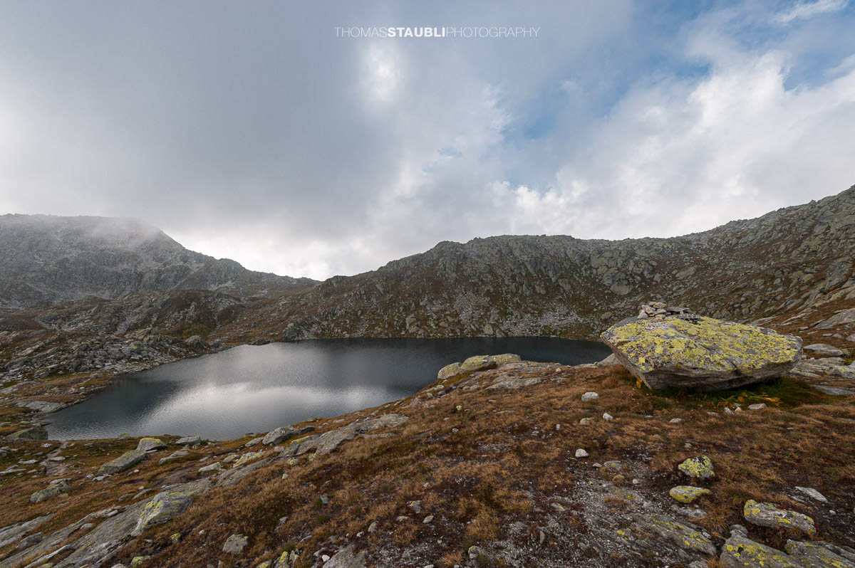 Laghi d’Orsirora nahe dem Gotthardpass, kleiner Hochgebirgssee in karger alpiner Felslandschaft unter wechselndem Himmel.