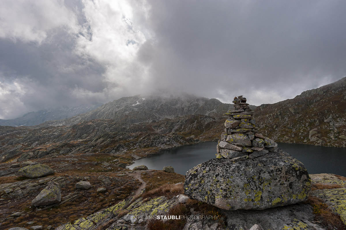 Laghi d’Orsirora nahe dem Gotthardpass, kleiner Hochgebirgssee in karger alpiner Felslandschaft unter wechselndem Himmel.