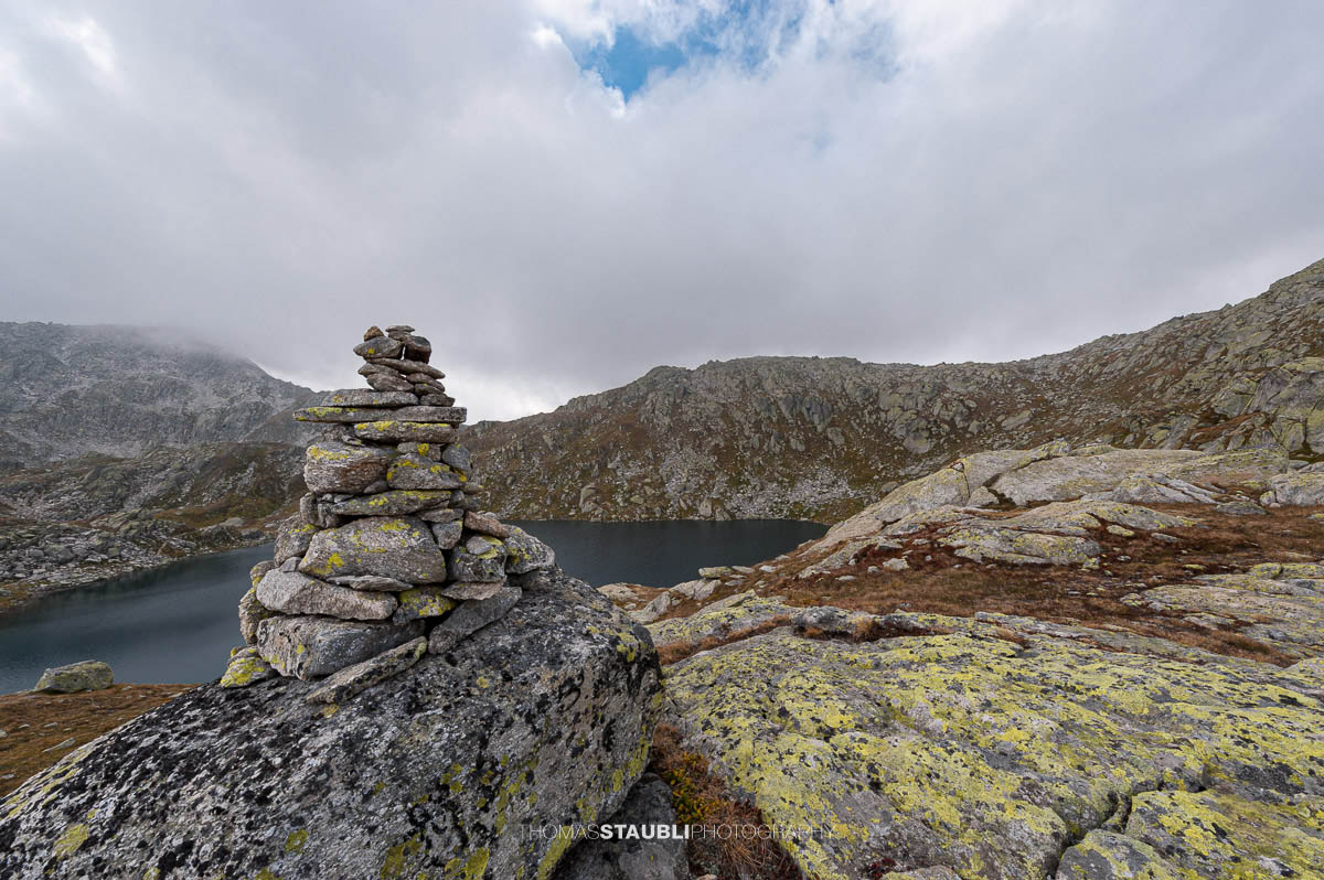 Laghi d’Orsirora nahe dem Gotthardpass, kleiner Hochgebirgssee in karger alpiner Felslandschaft unter wechselndem Himmel.